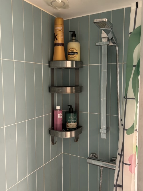 Stainless steel shower caddy in Duplex Marais bathroom with toiletries and hair care products, Paris apartment