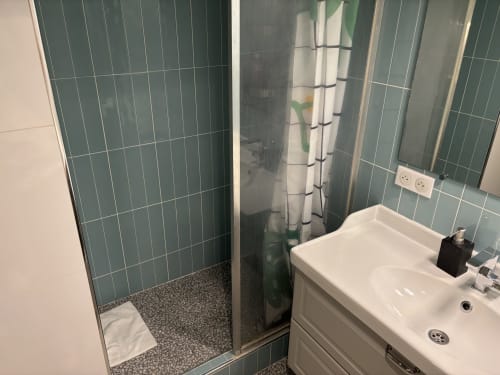 Modern bathroom in Duplex Marais apartment Paris with tiled shower enclosure, white sink vanity, and green tiled walls