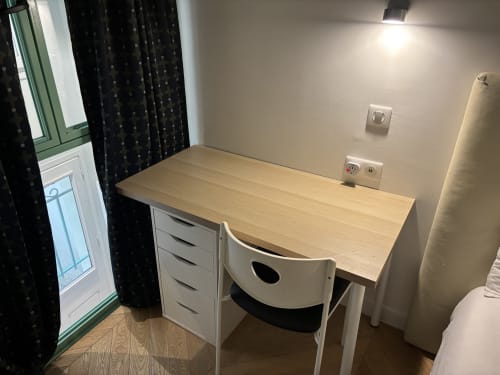 Modern workspace desk with wooden top, white chair, and drawers in Duplex Marais apartment, Paris hotel room with window and