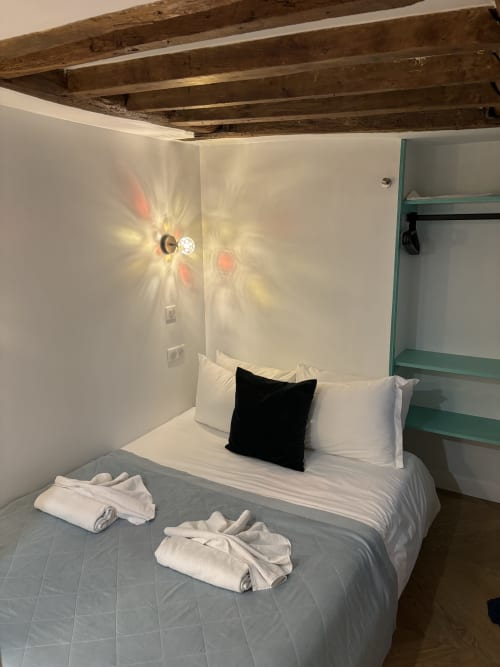 Cozy bedroom in Aldaro Duplex Marais apartment, Paris, with exposed wooden beams, white linens, and modern wall sconce