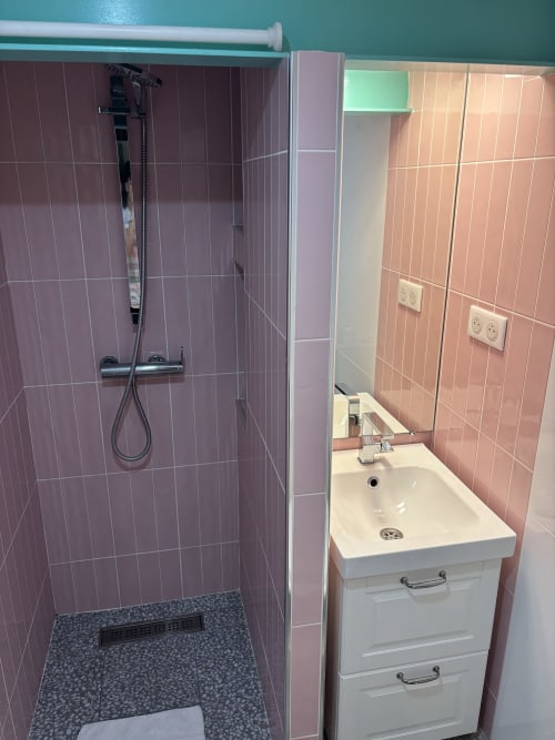 Modern bathroom in Paris Marais apartment with pink tiled shower enclosure, white vanity sink, and turquoise accent wall