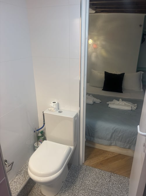 Compact bathroom in Duplex Marais apartment, Paris hotel with white toilet, sink, and adjacent bedroom view