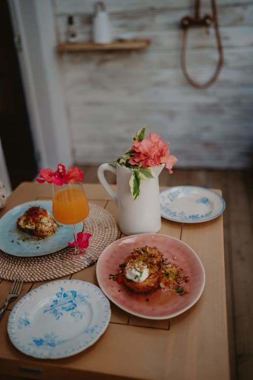 Table de petit-déjeuner élégante à Bleu Guesthouse avec fleurs roses, jus frais et cuisine gastronomique