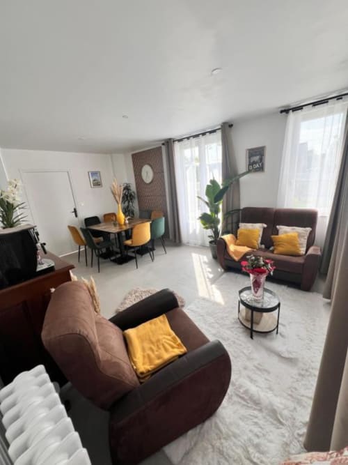 Chambre spacieuse et accessible à La Villa Cassinne avec canapés marron, coussins jaunes, coin repas et terrasse avec vue sur le jardin.