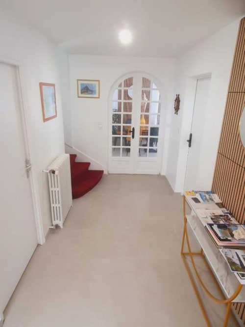 Couloir de chambre moderne et accessible à La Villa Cassinne avec sièges rouges, bibliothèque à arche blanche et sol beige