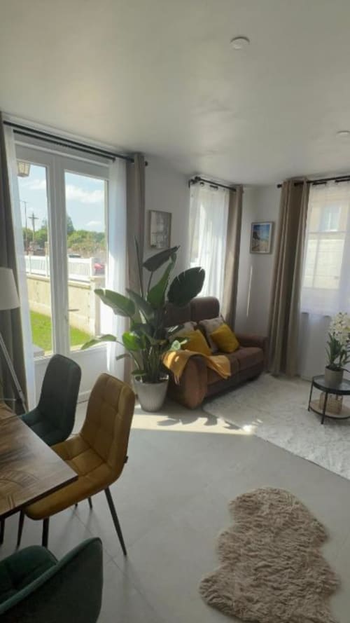 Chambre Deluxe lumineuse à La Villa Cassinne avec canapé marron, accents moutarde, plante en pot et vue jardin par les portes de terrasse