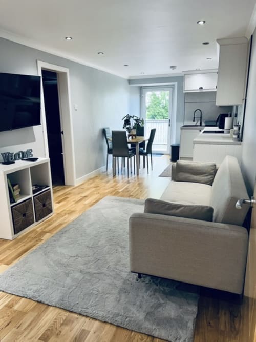 Modern open-plan living area at Whiteleys Cottages cottage in Dumbarton with gray sofas, dining table, kitchen, and garden