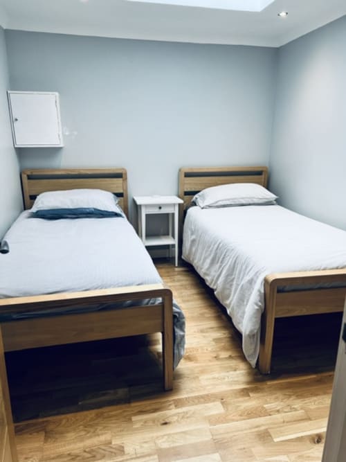 Twin bedroom with wooden beds, white linens, hardwood floors, and light blue walls at Whiteley's Cottages, Dumbarton
