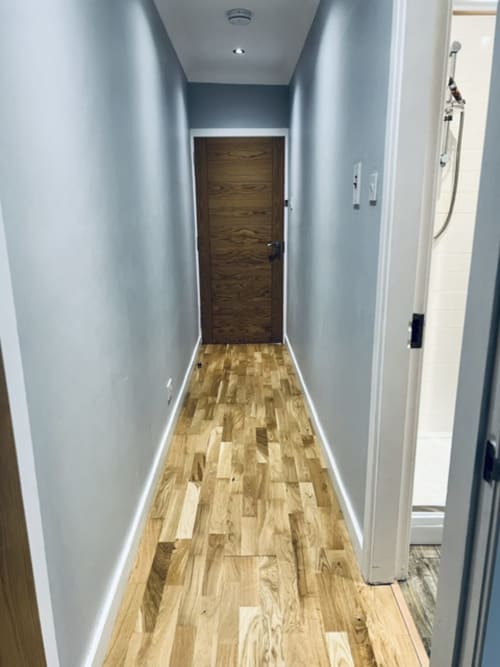 Modern hallway corridor in Whiteley's Cottages cottage with light wood flooring, pale blue walls, and dark wooden door at end
