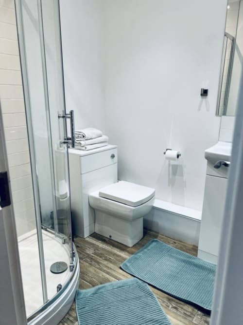 Modern bathroom in Whiteley's Cottages cottage with shower enclosure, toilet, sink, and wood-effect flooring with blue bath