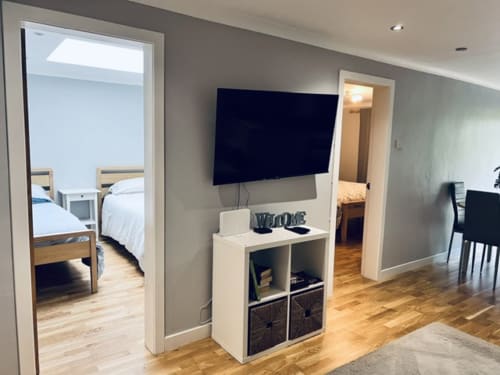 Modern living area in Whiteleys Cottages Dumbarton with flat-screen TV, white storage unit, hardwood floors, and doorways to