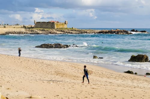 Surfistas na praia de Matosinhos com forte histórico, ondas e litoral rochoso sob céu azul