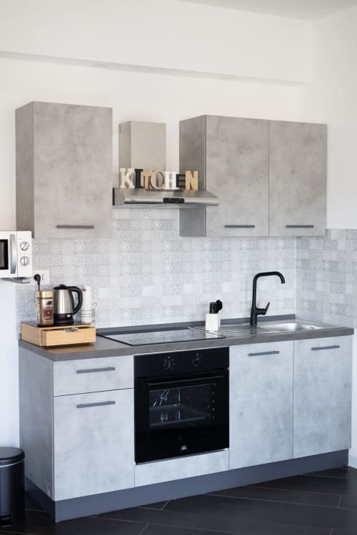Cucina moderna nell'appartamento deluxe Newhouse Bari con ante in cemento, piano cottura nero e rivestimento decorativo in piastrelle