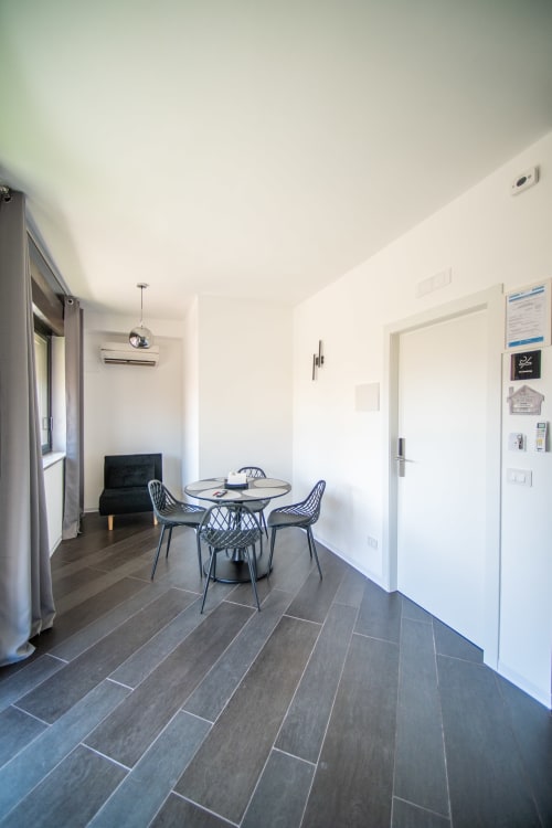 Moderna zona pranzo nell'Argiro Deluxe Apartment a Newhouse Bari con tavolo rotondo, sedie nere, pavimento in legno scuro e bianco