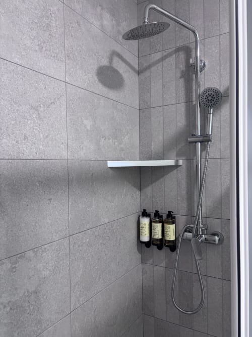 Modern shower at La Llar B&B in Carboneras with rainfall showerhead, handheld spray, white shelf, and toiletries dispenser