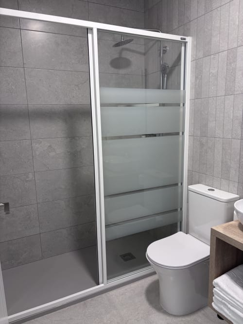 Modern bathroom in La Llar Carboneras with glass shower enclosure, toilet, and gray tile walls
