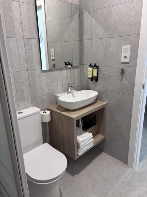 Modern bathroom with white vessel sink, wooden vanity, toilet, and gray tiled walls at La Llar hotel in Carboneras