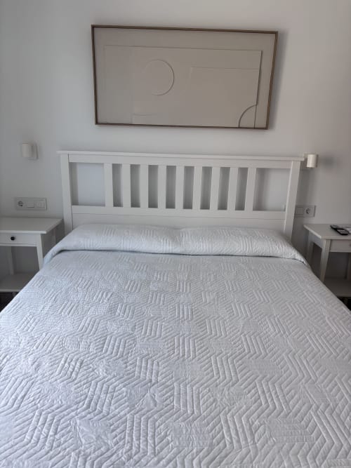 Bright bedroom with white wooden bed frame and quilted white bedding at La Llar, Carboneras. Nightstands on each side, framed