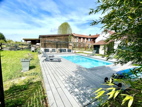 L'espace piscine du Paddock avec terrasse en bois, chaises longues et bâtiments en pierre à La Drenne