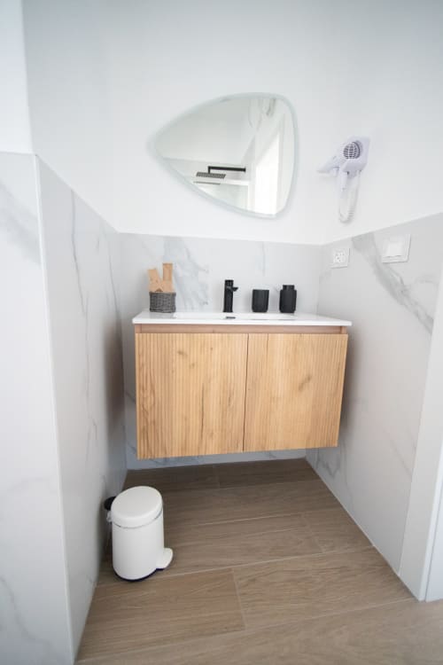 Bagno moderno a Newhouse Bari con vanity in legno, pareti in marmo bianco, specchio, ventilatore e cestino bianco