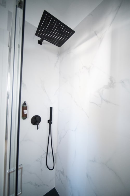 Moderni rubinetti doccia neri e soffione a pioggia in bagno con rivestimento in marmo all'hotel Newhouse di Bari