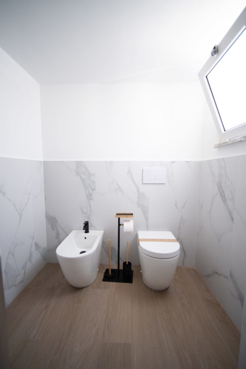Bagno moderno con arredi bianchi e pareti in marmo presso l'hotel Newhouse di Bari