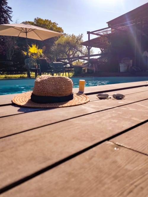 Chapeau de paille et lunettes de soleil sur la terrasse du Paddock B&B à La Drenne, avec piscine turquoise et coin détente