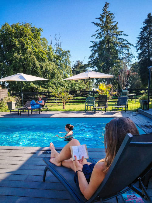 Femme lisant au bord de la piscine du Paddock B&B à La Drenne, France, avec baigneur et coin ombragé
