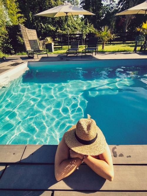 Personne au chapeau de paille se relaxant au bord de la piscine du Paddock B&B à La Drenne, France, avec eau turquoise cristalline et chaise longue