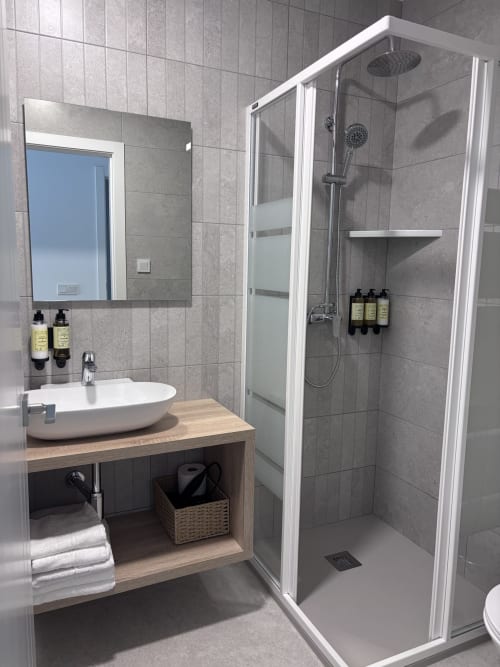 Baño moderno en La Llar de Carboneras con lavabo redondo blanco, paredes de azulejos grises, plato de ducha y equipamiento completo