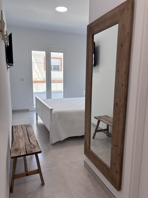 Dormitorio moderno en La Llar de Carboneras con espejo de marco de madera, cama blanca, acceso a balcón y vistas al mar