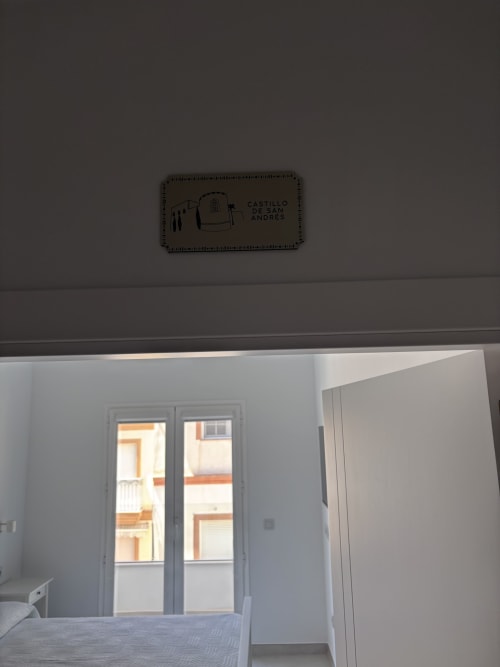 Bedroom at La Llar with sea view, double bed, glass balcony doors, and Castillo de San Andrés plaque above