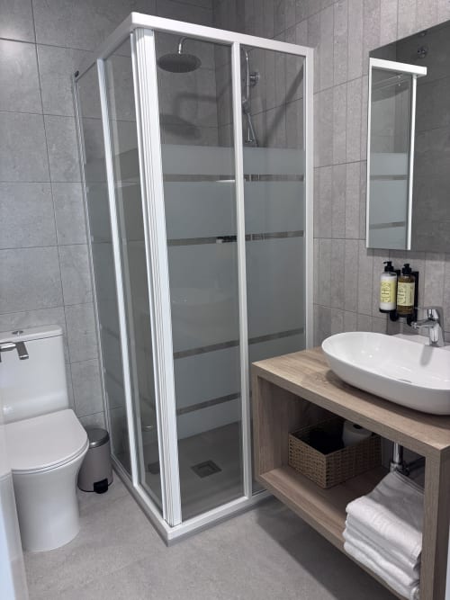 Modern bathroom at La Llar B&B in Carboneras with shower enclosure, vessel sink, and wooden vanity storage.