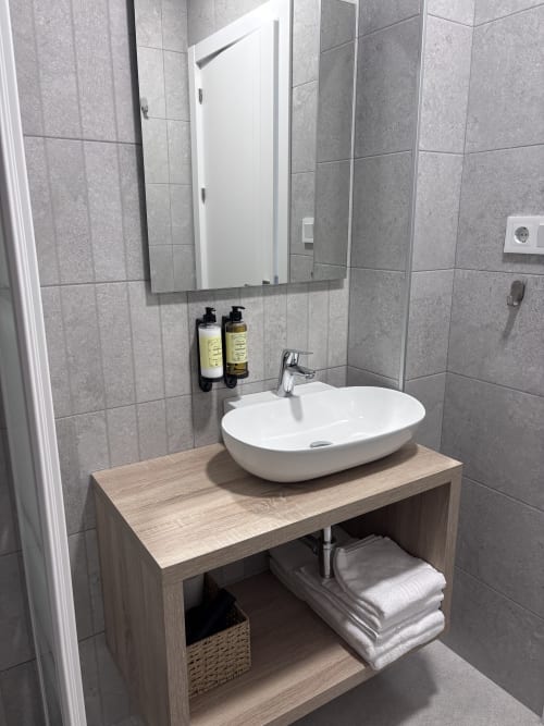Modern bathroom vanity with white vessel sink, wooden cabinet, mirror, and grey tile walls at La Llar, Carboneras