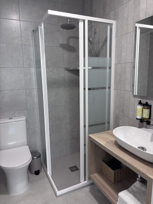 Modern bathroom in La Llar B&B Carboneras with glass shower enclosure, white sink, toilet, and wooden vanity
