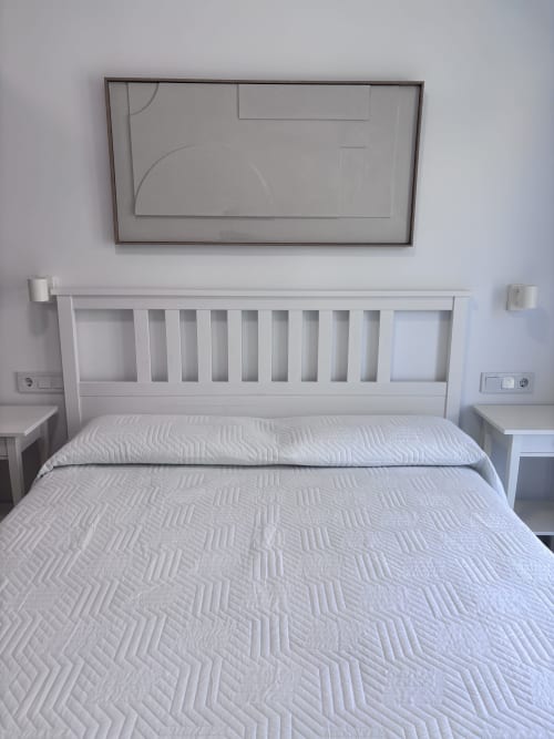 Modern white bed with geometric quilt in La Llar sea-view room, Carboneras, with mounted TV above