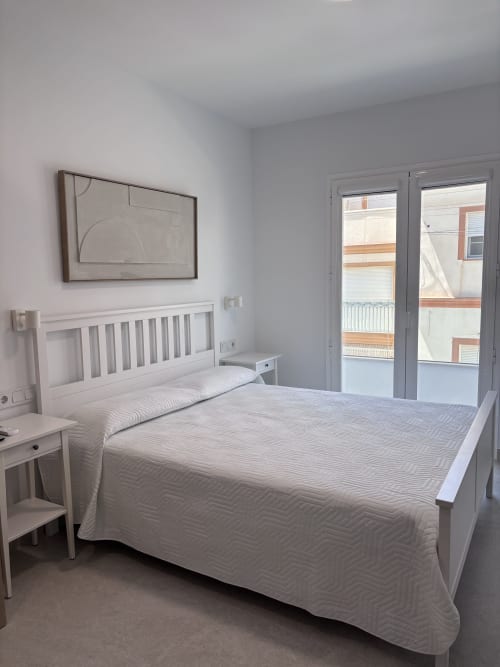Bright modern bedroom at La Llar Carboneras B&B with white bed, sea view doors, abstract artwork, and minimalist decor