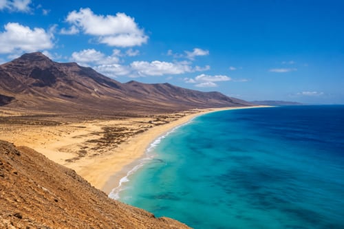 Playa turquesa con arena dorada, montañas volcánicas y cielo azul despejado cerca del Hotel Rural El Cabo en Villaverde