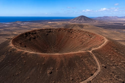 Paisaje de cráter volcánico cerca del Hotel Rural El Cabo en Lanzarote, con vistas al océano y picos distantes