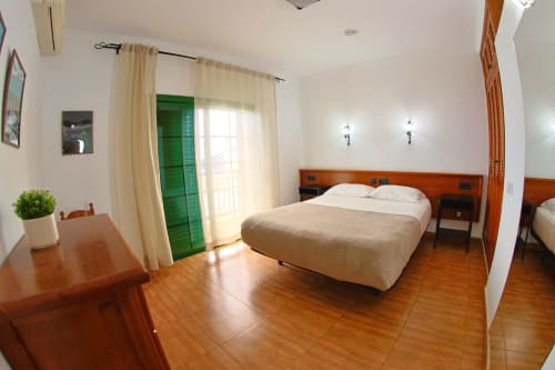 Amplio dormitorio de apartamento con cama de madera, piso de madera, puerta con persianas verdes y balcón con vistas al mar en Apartamentos La