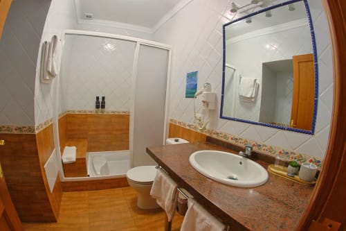 Baño moderno en Apartamentos La Palmera con azulejos blancos, tocador marrón, lavabo blanco y espejo con azul