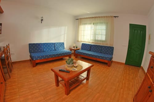 Amplia sala de estar en Apartamentos La Palmera con dos sofás azules, muebles de madera y piso de azulejos naranjas en La