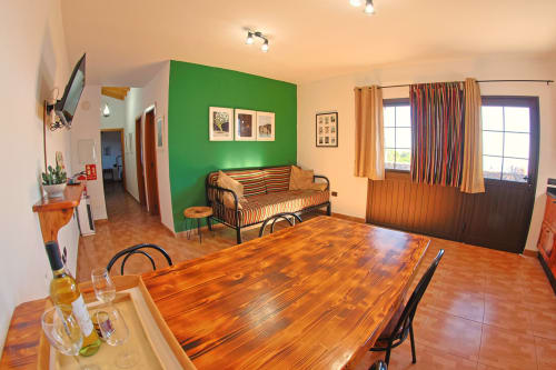 Open-plan living area in Casa La Tabona cottage with wooden dining table, striped sofa, green accent wall, and sea views at