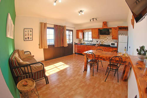 Open-plan living area at Casa La Tabona cottage with wooden dining table, kitchen, sofa, and sea views in La Frontera