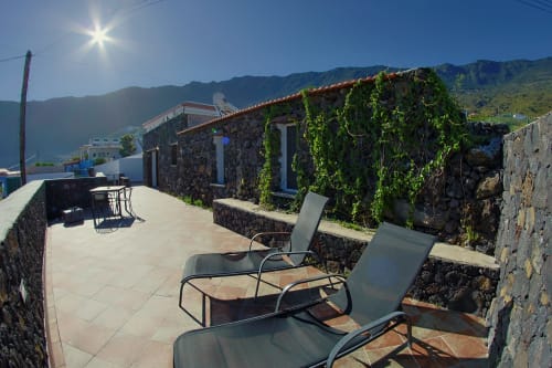 Sunny terrace at Casa La Tabona cottage in La Frontera with sea and mountain views, lounge chairs, and ivy-covered stone