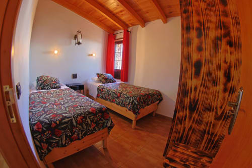 Twin bedroom with colorful patterned bedspreads at Casa La Tabona cottage in La Frontera, featuring wooden beams and red