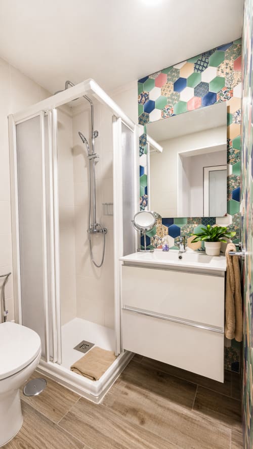Modern bathroom with colorful hexagonal tile accent wall, white vanity sink, and glass shower enclosure in Apartamento Severo