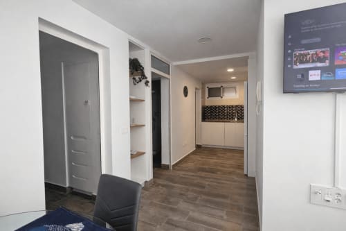 Modern apartment hallway with wooden flooring, white walls, gray door, wall-mounted TV, and shelving in La Aldea vacation