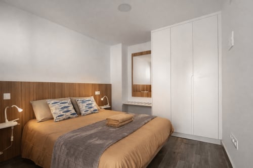 Modern bedroom in Apartamento Severo 1 at Playa de La Aldea with wooden headboard, gold bedding, white wardrobes, and mirror