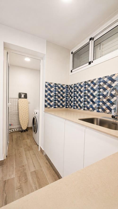 Modern laundry room with white cabinets, patterned backsplash, sink, and washer in La Aldea apartment
